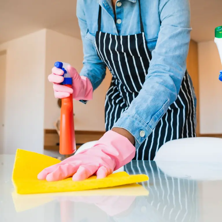 Hand im Reinigungshandschuh wischt mit einem gelben Tuch eine glänzende Oberfläche