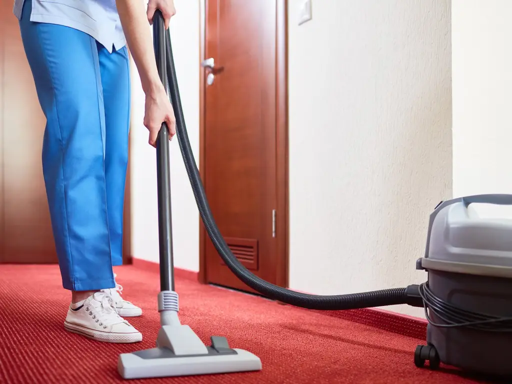 Reinigungskraft saugt den Teppich in einem Hotelflur